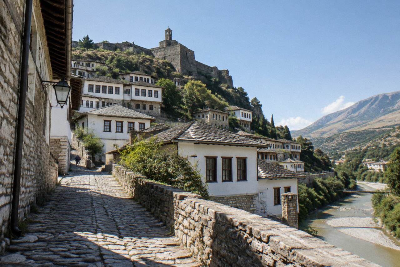 White Ottoman houses stacked on a hillside above a river in an Albanian town