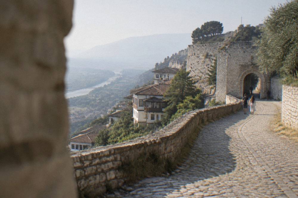 Cobblestone lane curving up toward a stone castle gateway in Berat