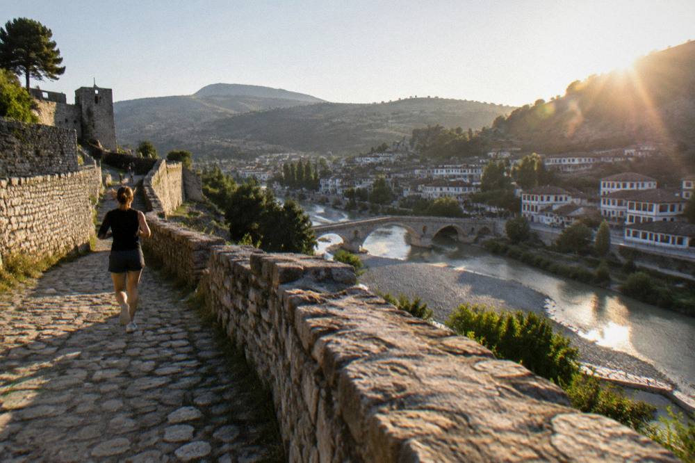 Sunlit white houses and a stone bridge over a river in Berat with clear sky