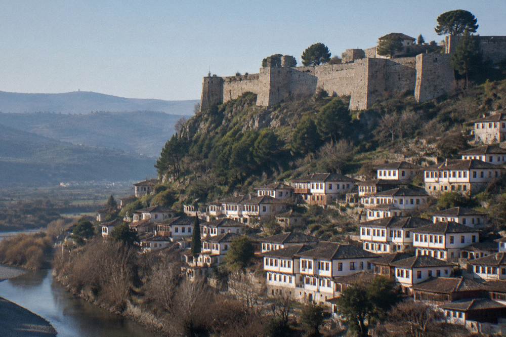 White Ottoman houses of Mangalem stacked on a hillside below Berat Castle under a clear morning sky