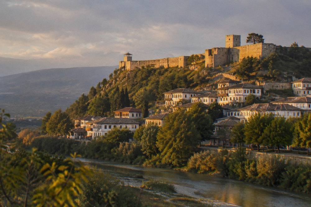 Golden late afternoon light on the stone walls and towers of Berat Castle seen from the valley