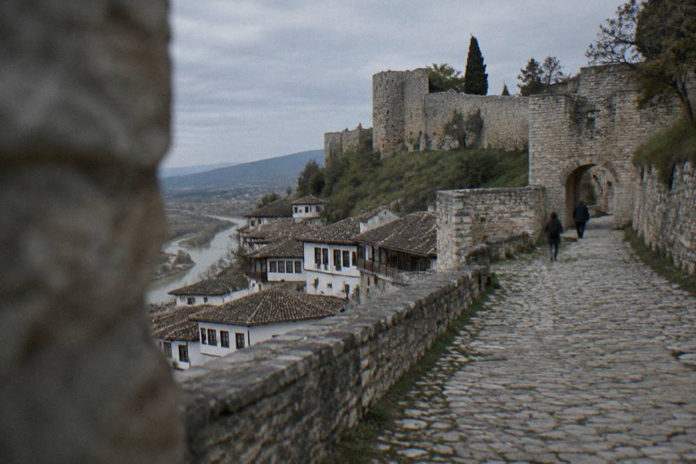 The steep cobbled lane climbing toward the stone gate of Berat Castle in soft morning light