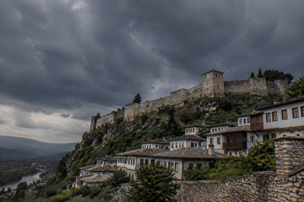 Dark storm clouds gathering above the stone towers of Berat Castle before an afternoon rain shower