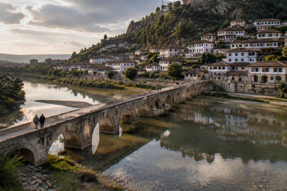 The Gorica Bridge and stone houses of Berat reflected in the calm Osum River at dusk