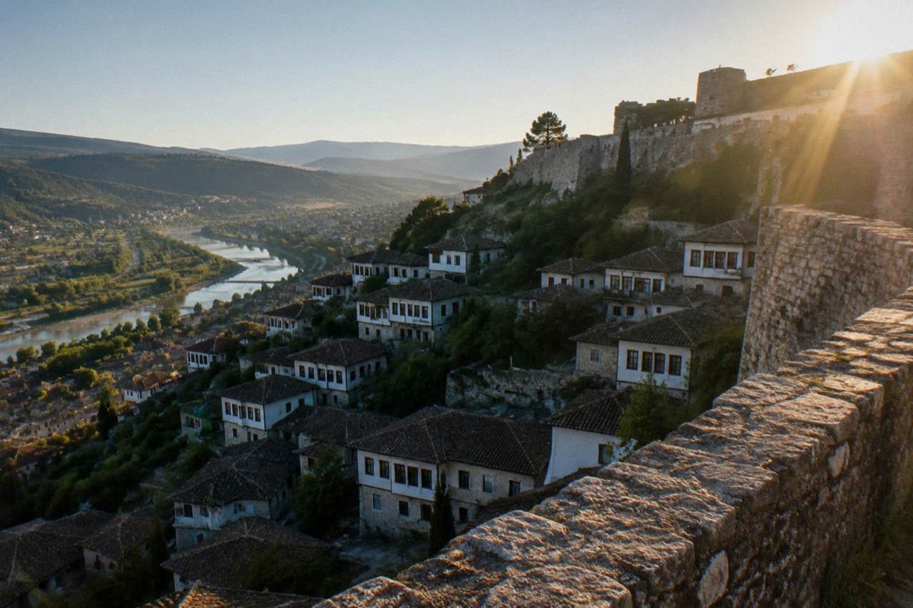 White Ottoman houses of Mangalem stacked on a hillside below Berat Castle under a clear morning sky