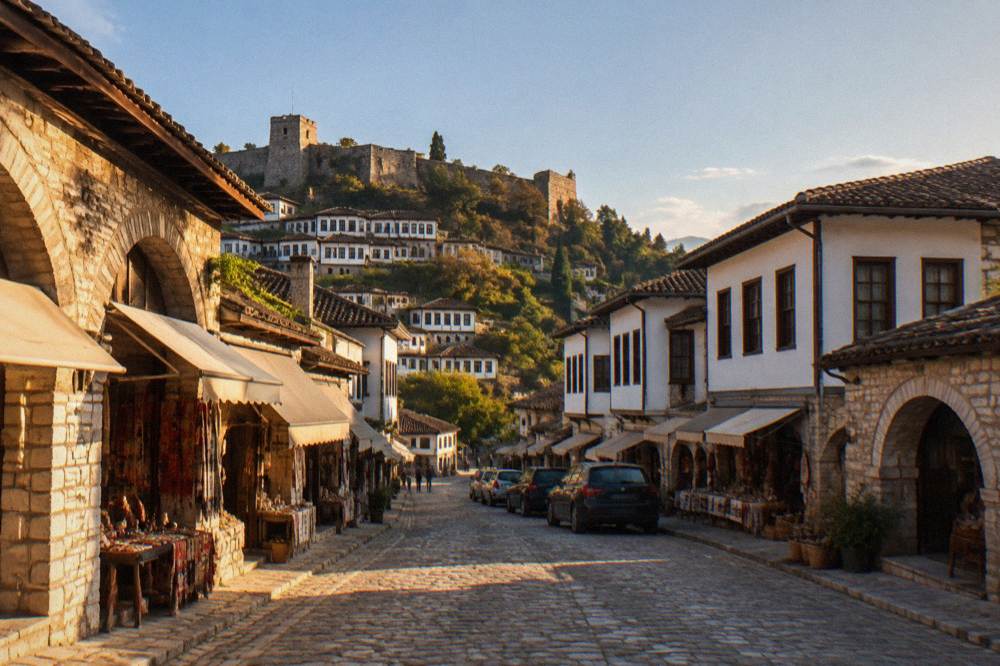 Narrow stone street with parked cars below the white Ottoman houses of Berat old town