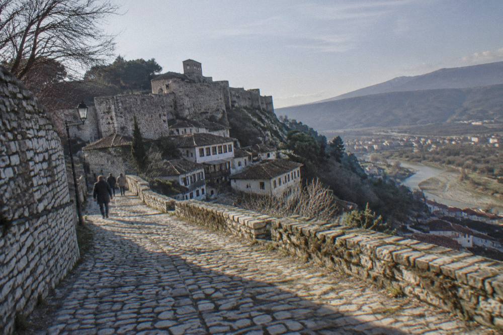 Stone cobblestone road climbing toward the walls and towers of Berat Castle