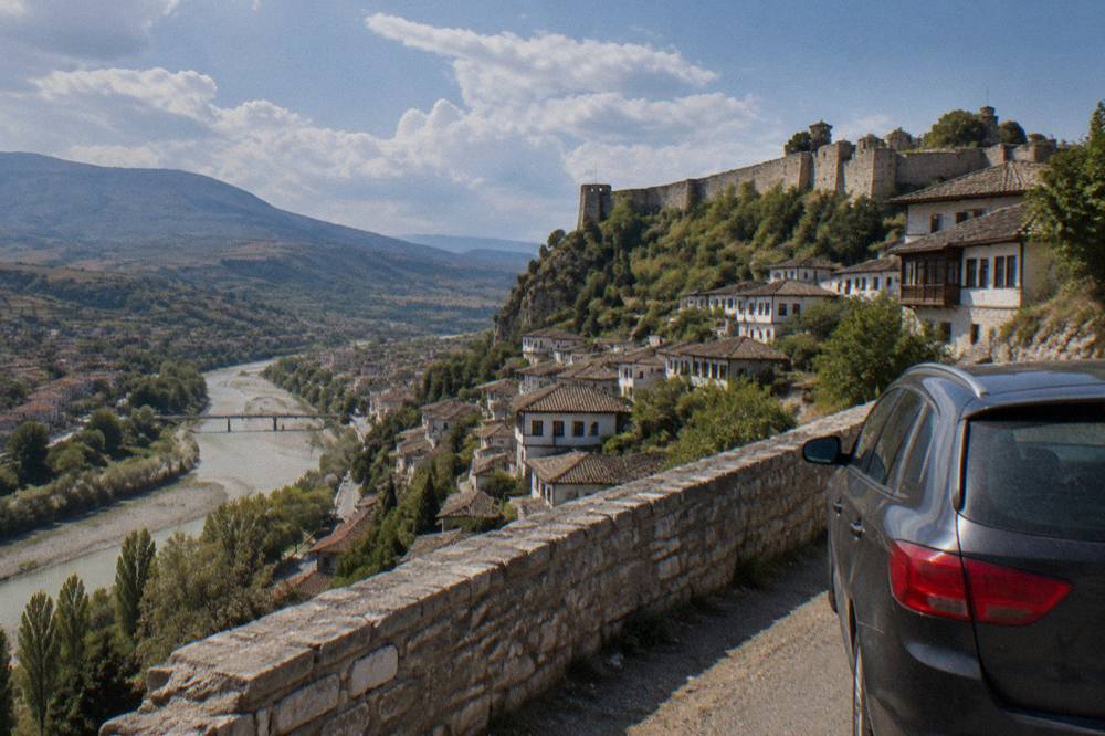 Car parked beside a stone wall on a hillside road overlooking Berat and the Osum valley