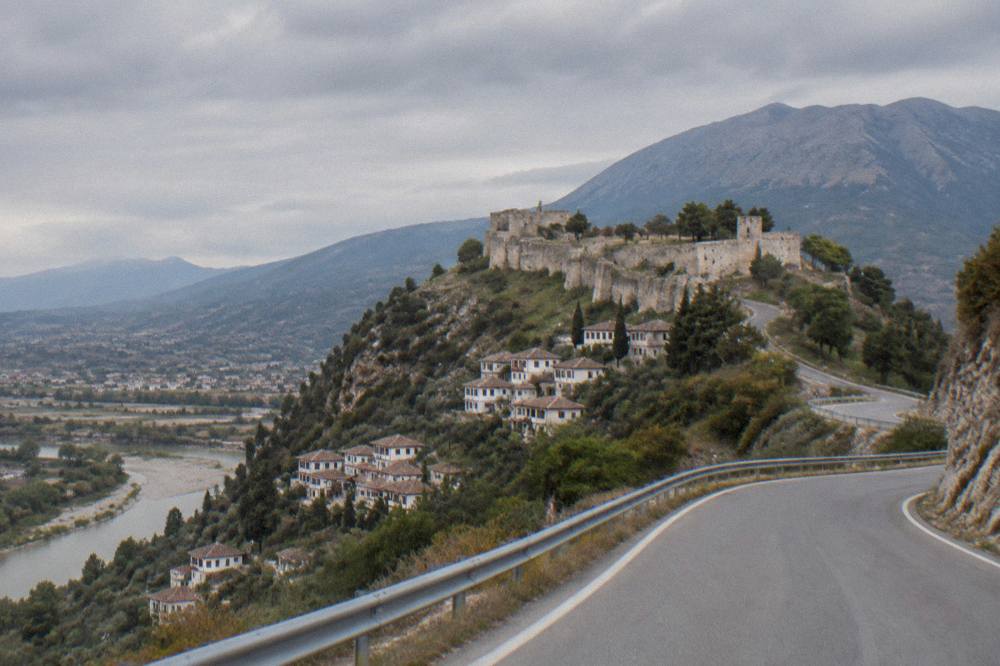 Empty winding mountain road with new guardrails climbing toward Mount Tomorr