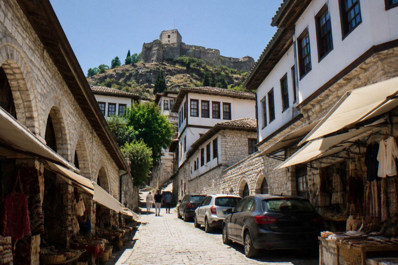 Narrow stone street with parked cars below the white Ottoman houses of Berat old town