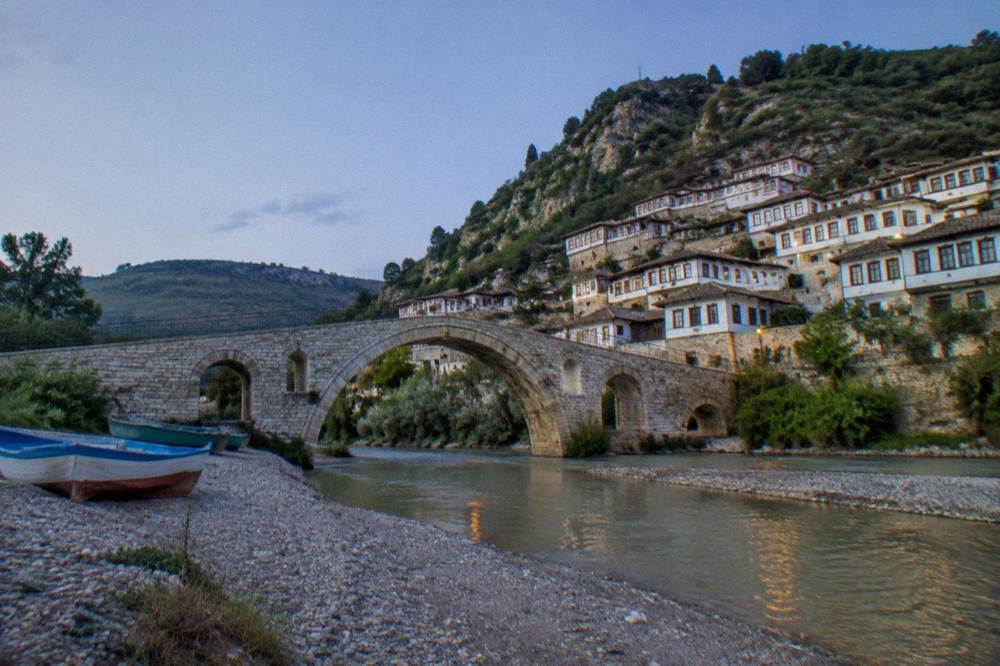Stone bridge over a river with white Ottoman houses climbing a hillside behind it