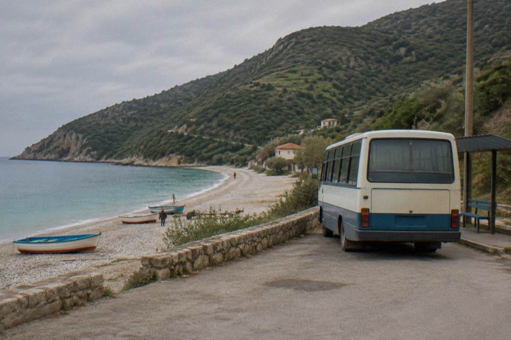 Small regional bus parked at a roadside terminal with hills in the background