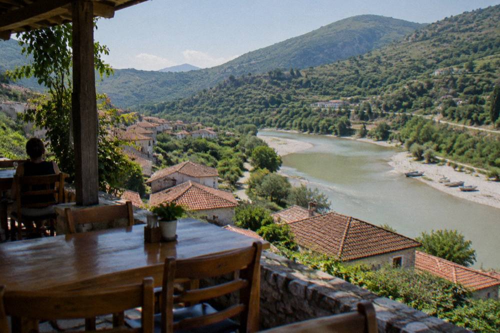 Guesthouse terrace with wooden tables overlooking tiled rooftops and a river valley