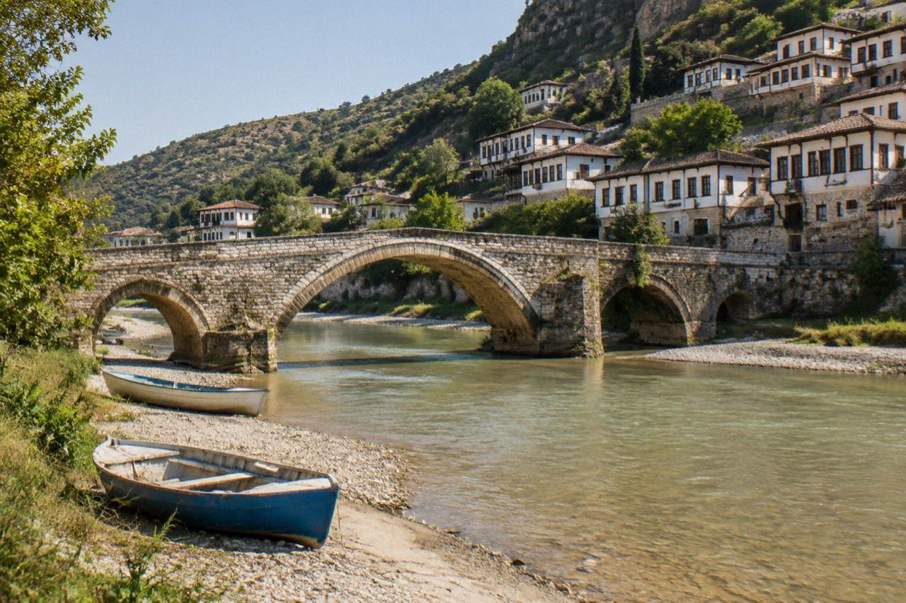 Stone bridge over a river with white Ottoman houses climbing a hillside behind it