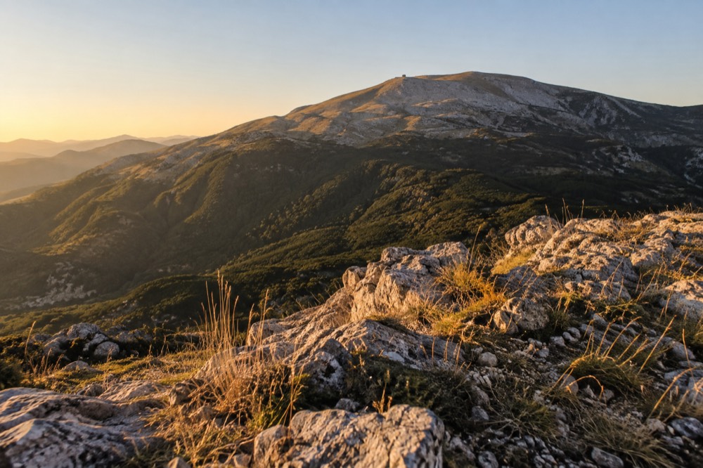 Mountain slopes of Tomorr rising above forested ridgelines under a clear sky
