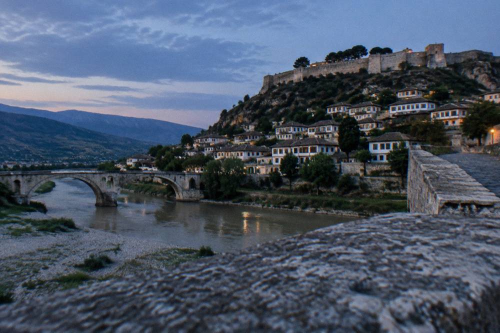 Old stone bridge arching over a wide river toward a hillside of houses