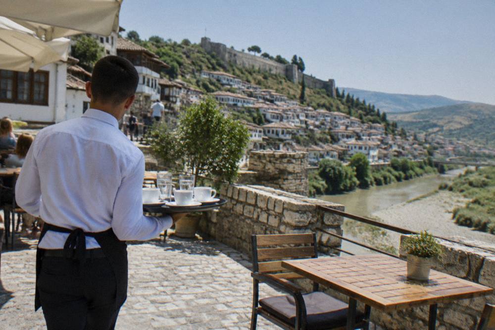 Waiter carrying a tray of coffee cups to an outdoor table on a sunny street