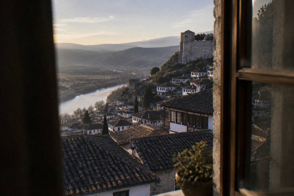 Guesthouse windows overlooking the tiled rooftops of Berat at sunset