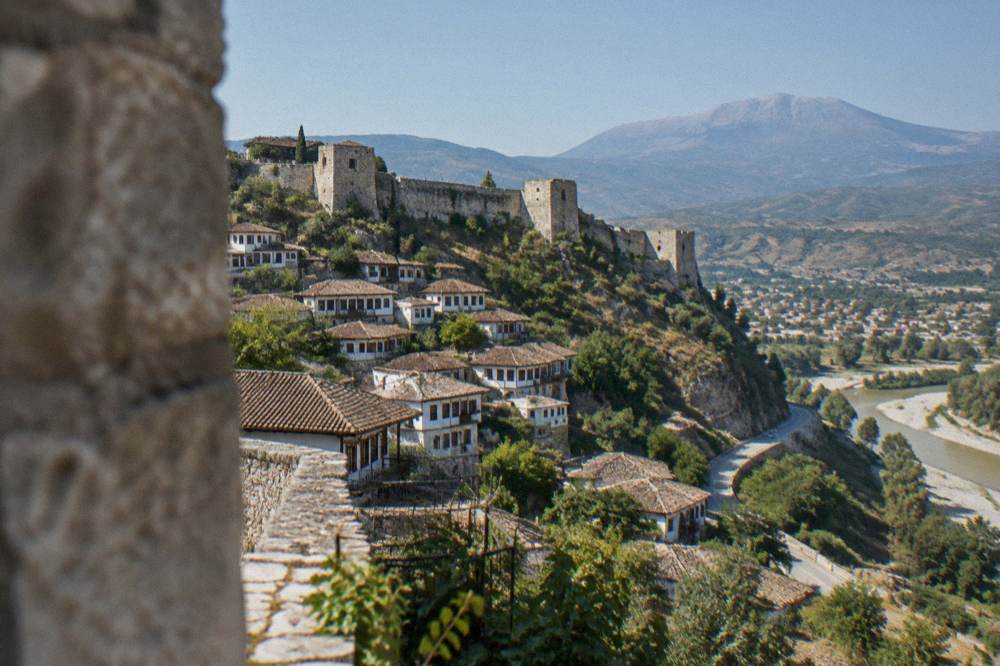 A country road winding through green hills toward Berat with Mount Tomorr in the distance