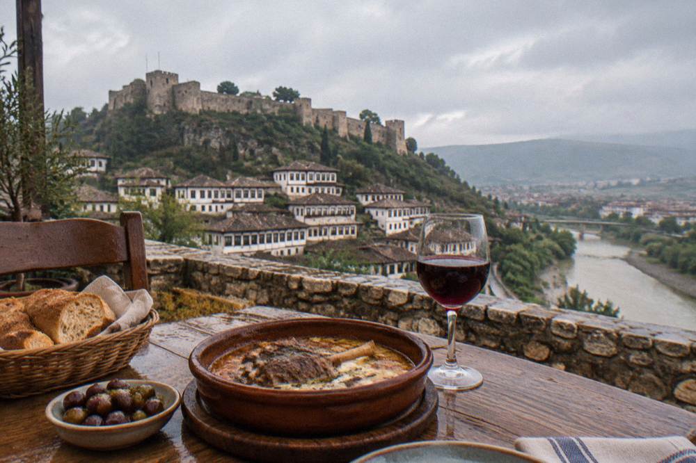 A rustic wooden table in a Berat restaurant set with a lamb and yogurt casserole, fresh bread, olives and a glass of red wine