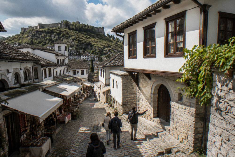 A small group walking a cobbled lane between whitewashed Ottoman houses with a guide gesturing toward a stone doorway