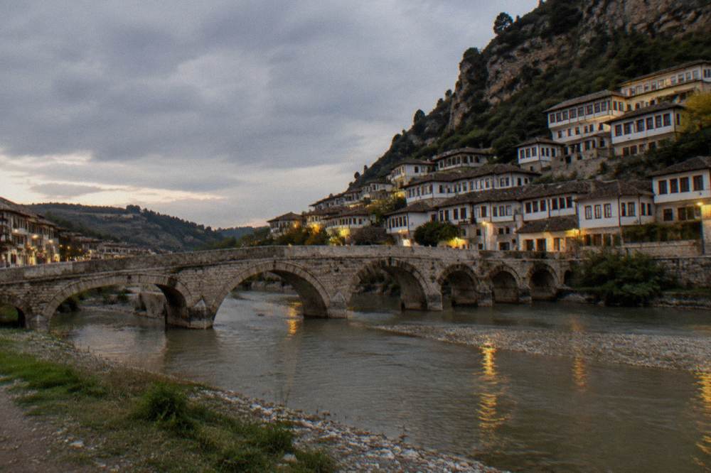 Gorica Bridge over the Osum River lit in the evening with houses on both banks