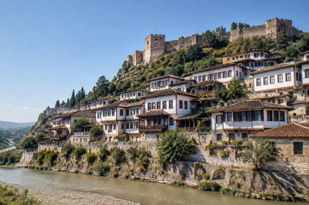White Ottoman houses stacked on a hillside above a river in Berat, Albania