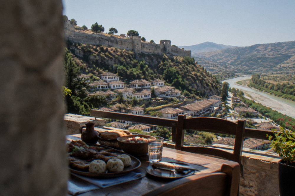 A table of traditional Albanian food with rice dumplings, grilled meat and bread on a terrace.