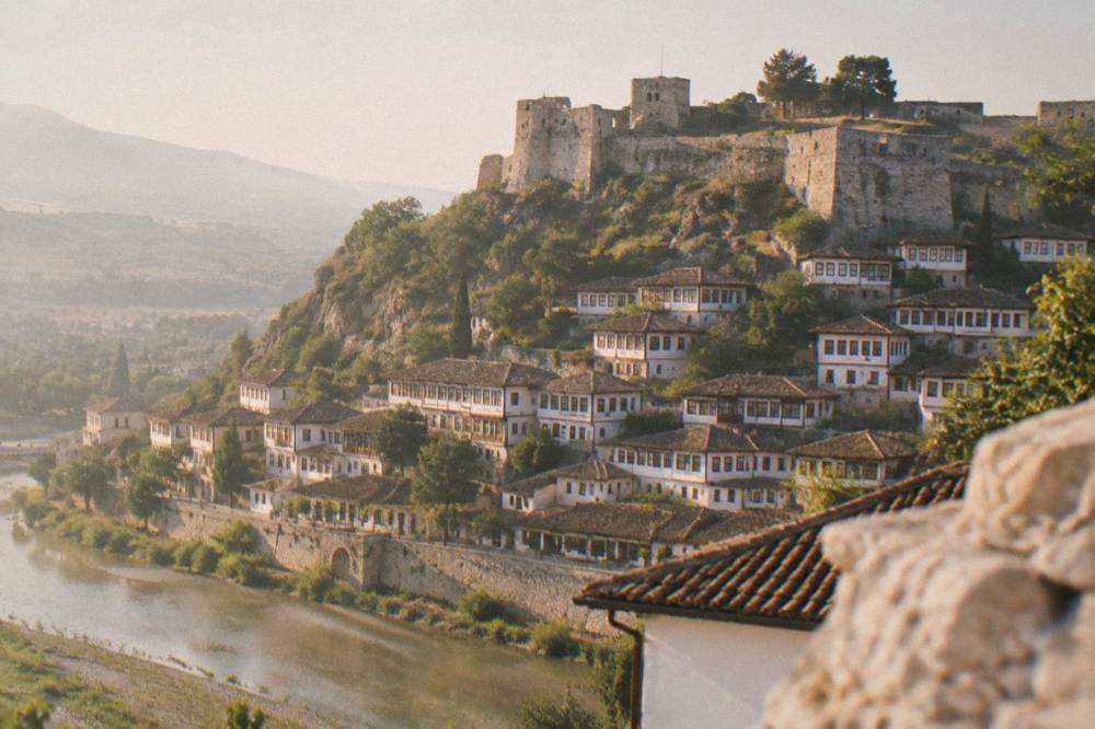 Rows of white Ottoman houses with many windows stacked above the Osum River in Berat at golden hour