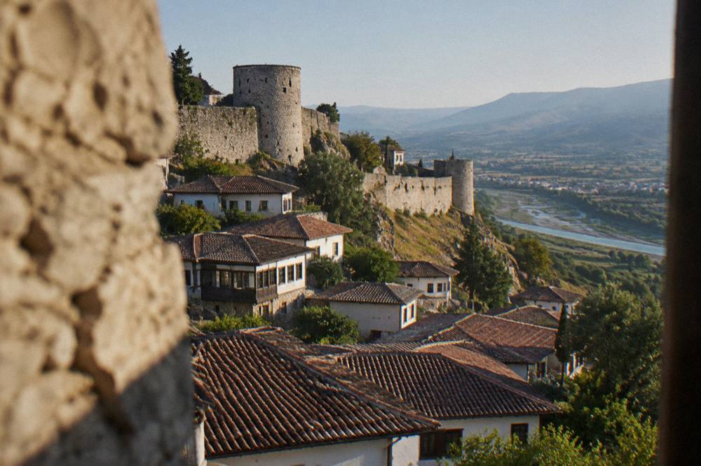 Stone fortress walls and round towers of Berat Castle on a hilltop above red tiled rooftops