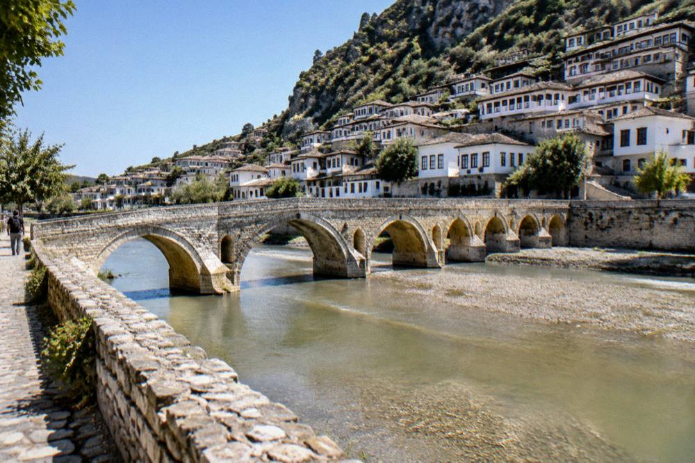 Stone Gorica Bridge arching over the green Osum River with white houses on both banks
