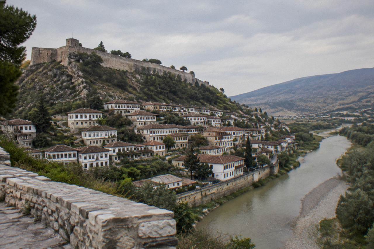 Rows of white Ottoman houses with many windows stacked above the Osum River in Berat at golden hour