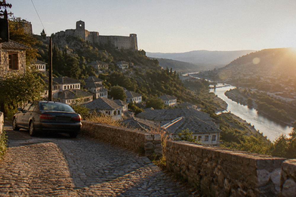 A car parked on a hillside road overlooking a river valley and town rooftops
