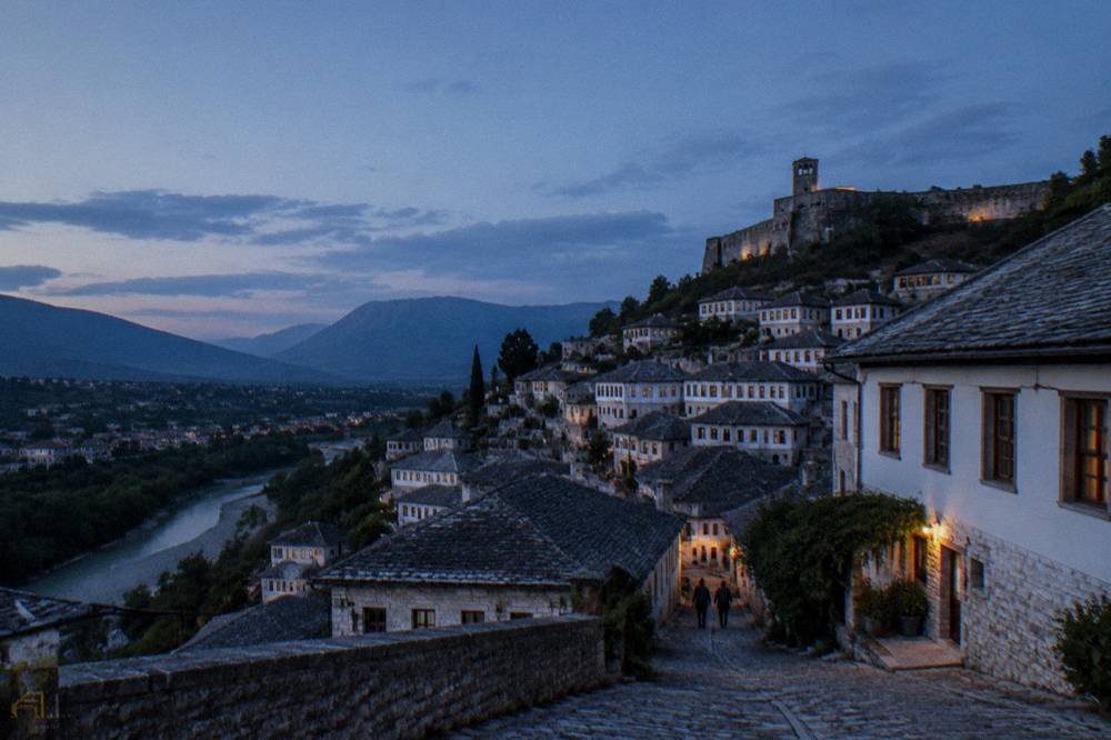 Rows of windows on white houses climbing a hillside beneath a fortress wall
