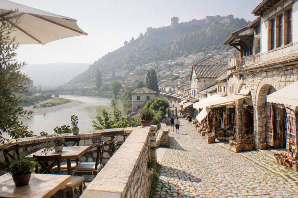 A stone guesthouse terrace with tables overlooking a river and old town rooftops