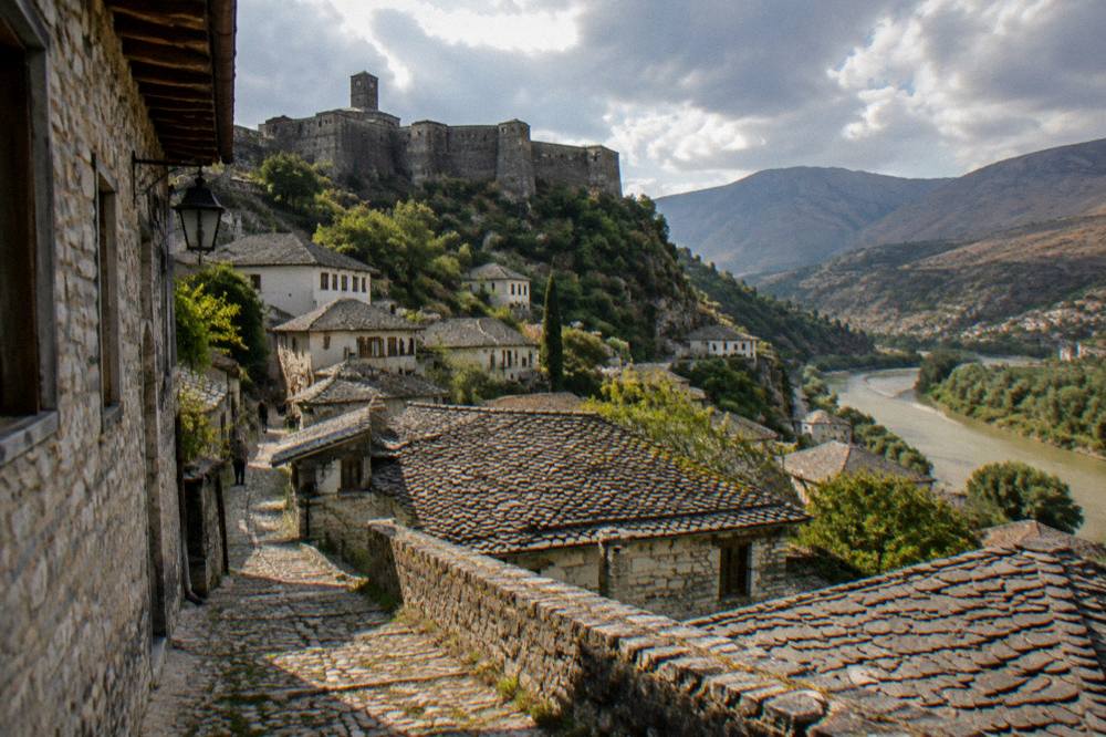 Grey stone houses with slate roofs on a steep hillside below a fortress