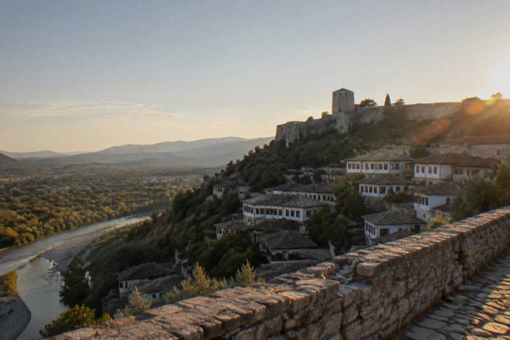 Stone castle walls and tower above rooftops in Berat at golden light