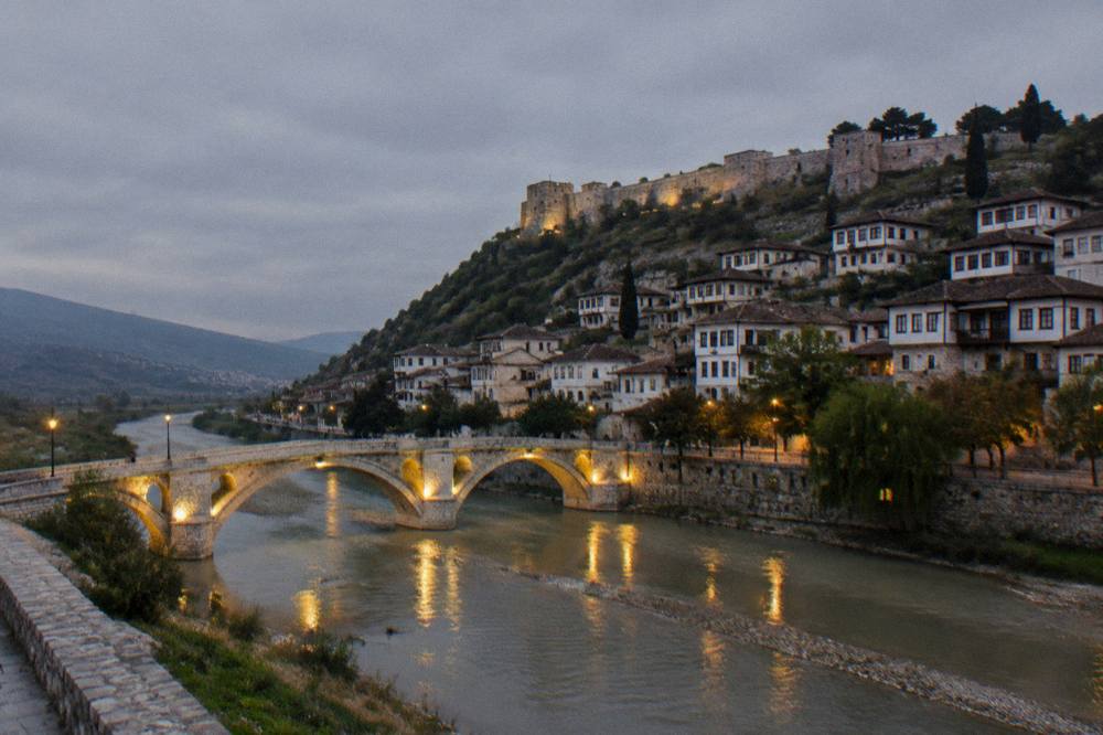 Evening view of a floodlit stone bridge and river reflections in a small town
